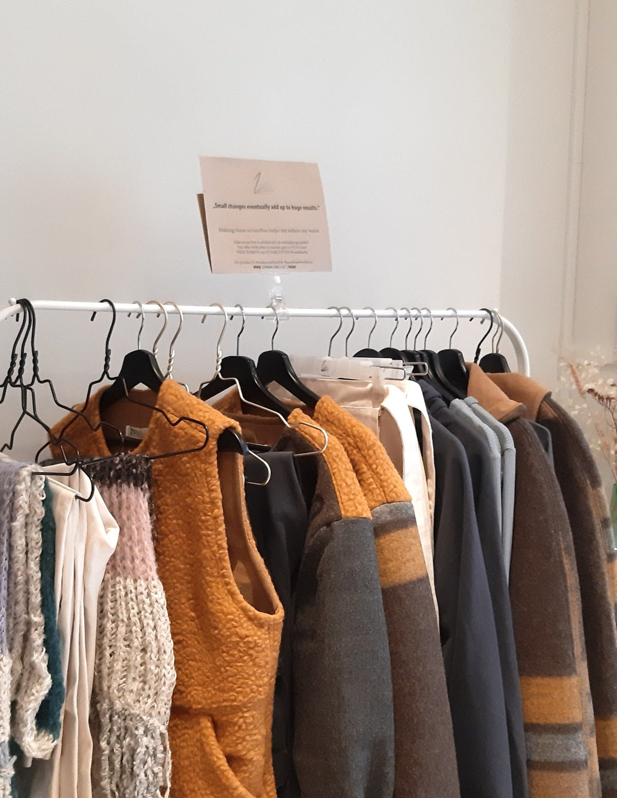 Kledingrek met ZWAAN-items in oker, bruin en grijs, met een bordje met het ZWAAN-logo