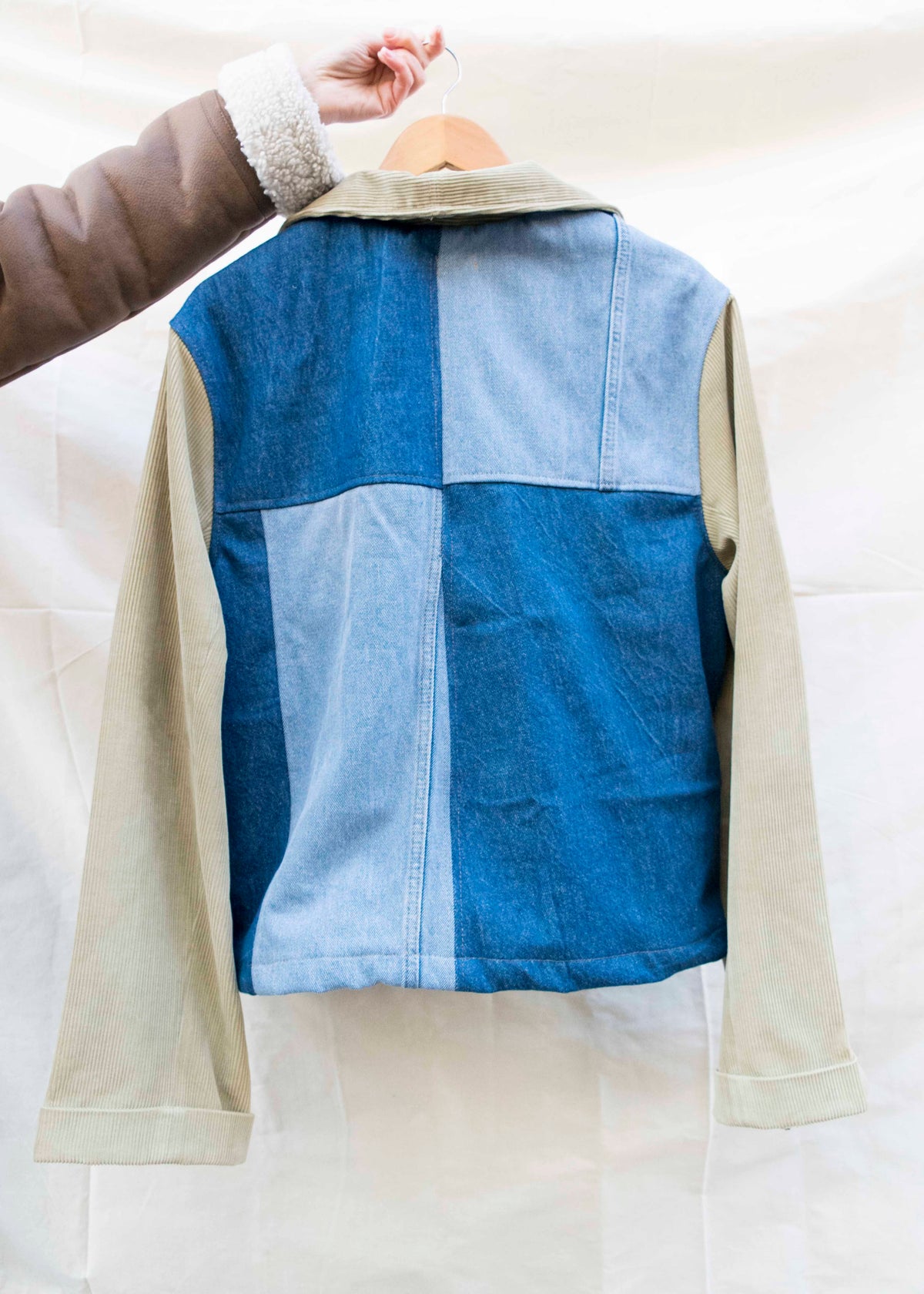 Achterkant van een patchworkjas van licht en donker denim met beige mouwen, aan een hanger