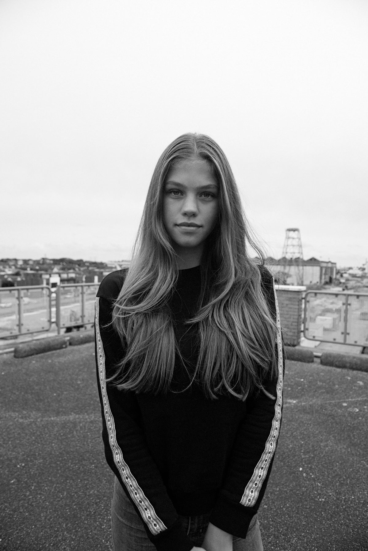 Zwart-witfoto van een vrouw met lang haar in een zwarte Basic sweater met schortenbont op de mouwen, op een dak