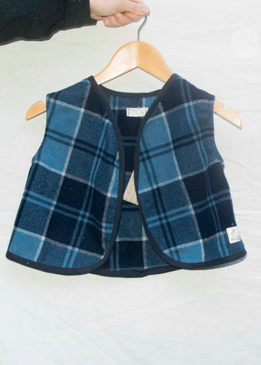 Mini gilet in blauwe ruit van restlappen wol met donkerblauw biasband, vooraanzicht op hanger
