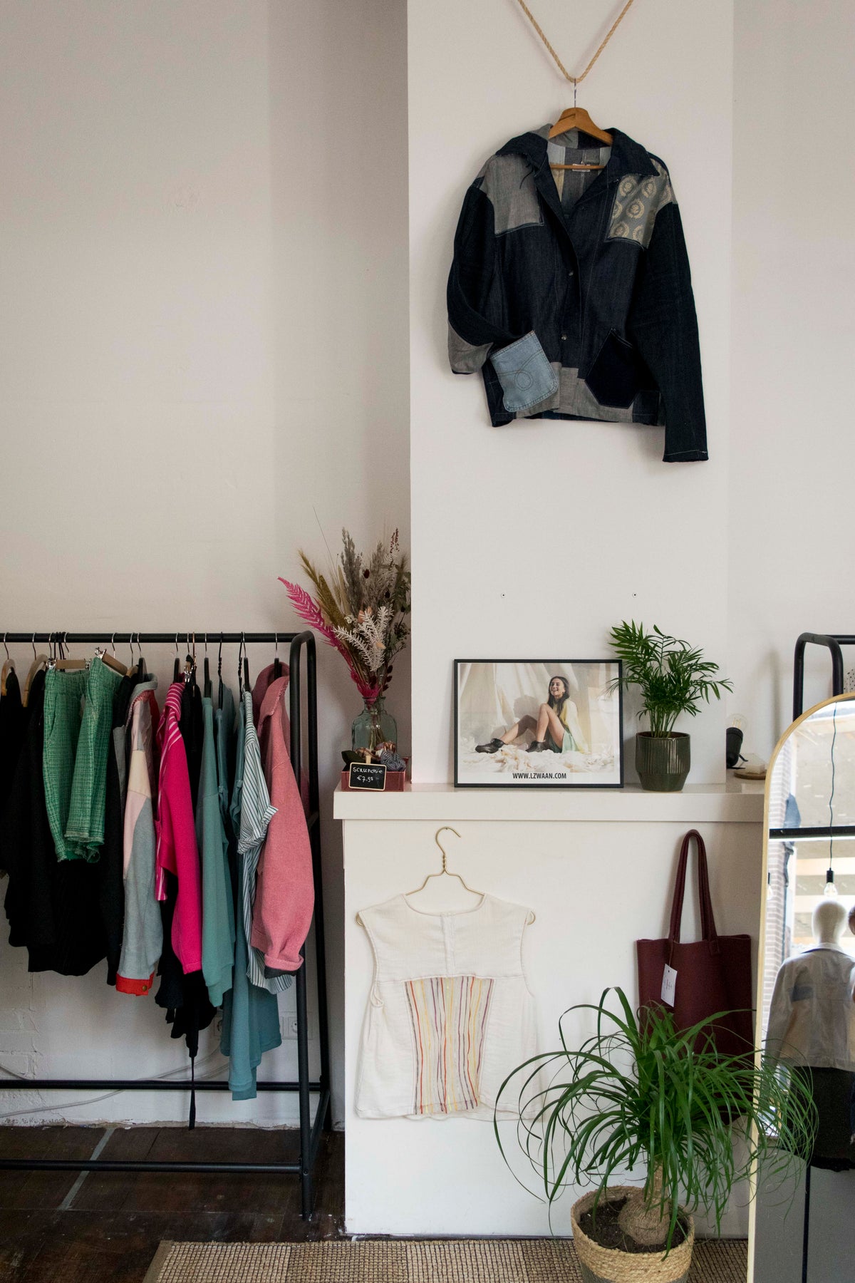 Interieur van de ZWAAN store met kledingrekken, een jasje aan de muur, planten en een spiegel