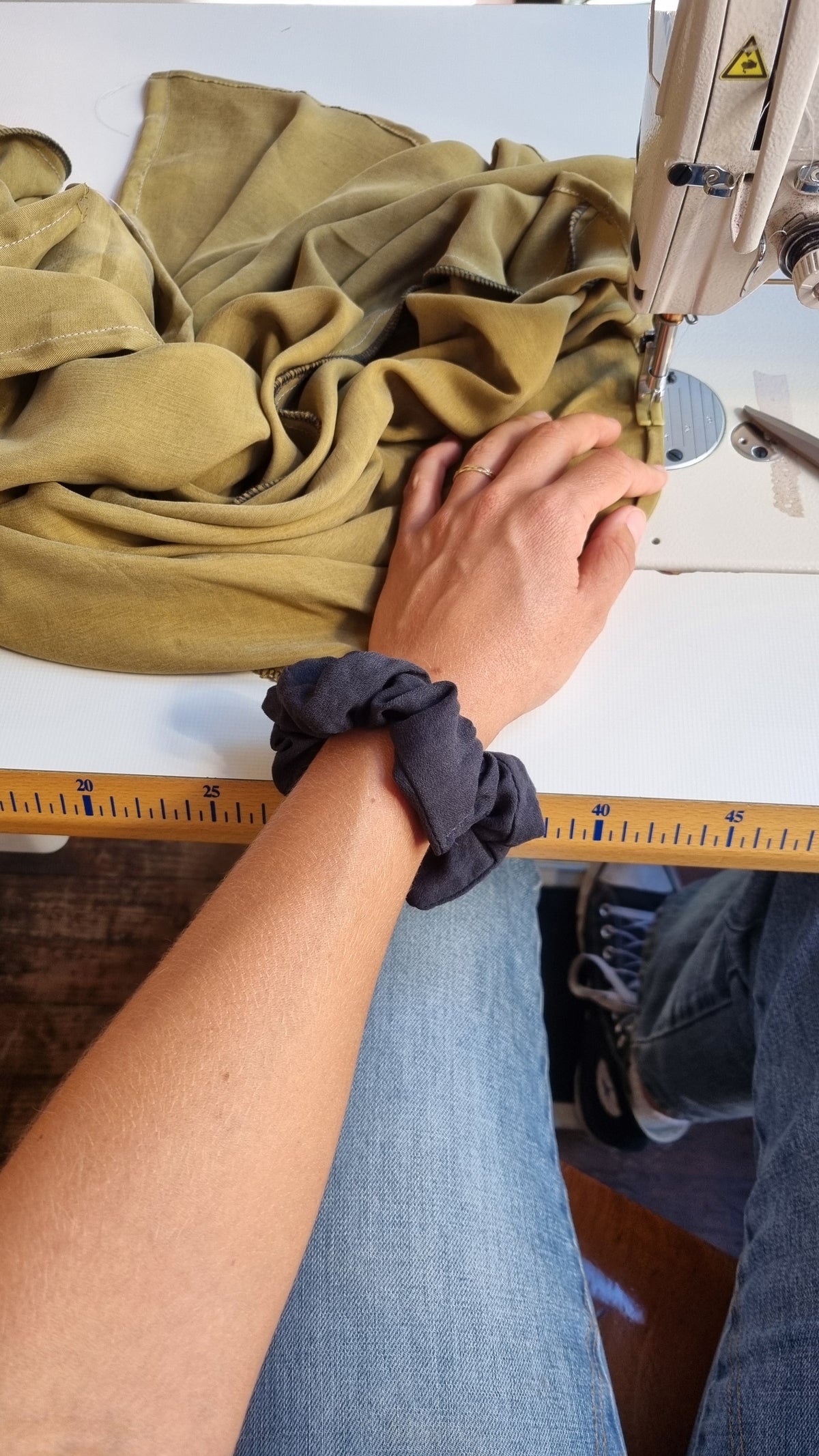 Hand met scrunchie bij een naaimachine en een stapel olijfgroene stof